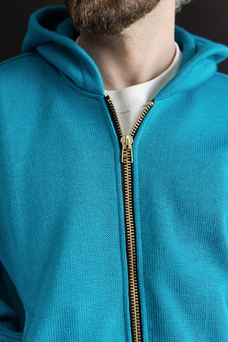 Close-up front view of aqua full-zip moto hoodie on male model, showing zipper detail and knit texture.