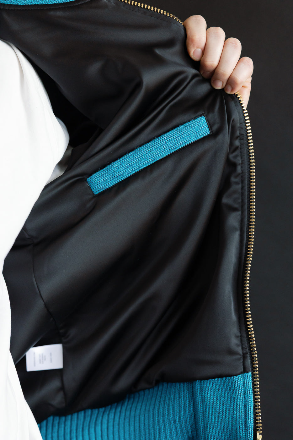 Close-up of male model holding open aqua moto hoodie, showing inside front left pocket and fabric details.