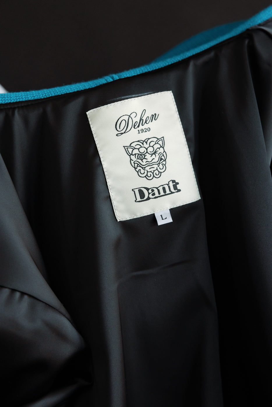 Close-up of interior neck area, showing size L woven tag and inner label on aqua full-zip hoodie.