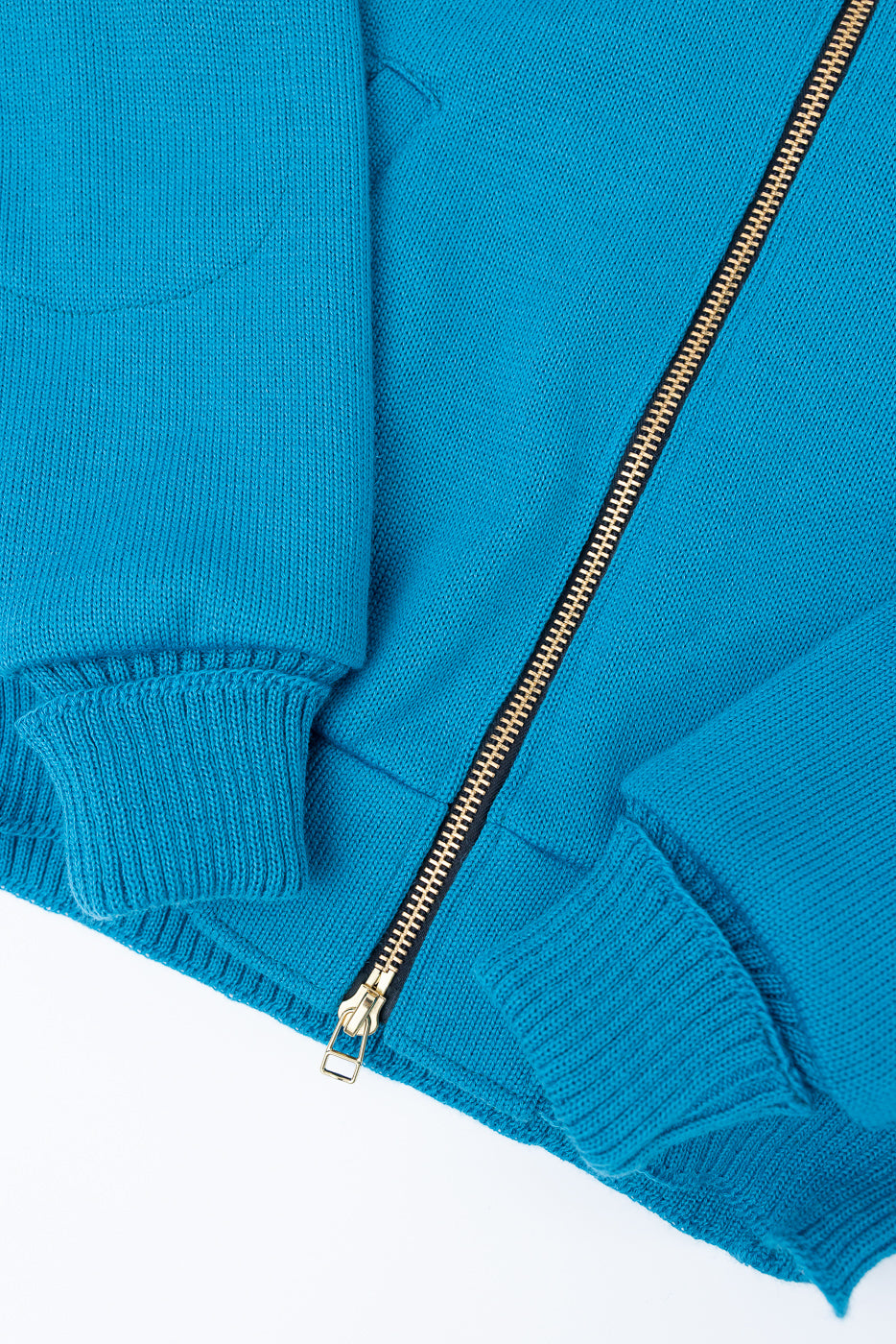 Close-up of aqua zip-up moto hoodie front hem, metal zipper, ribbed cuffs and knit fabric texture.