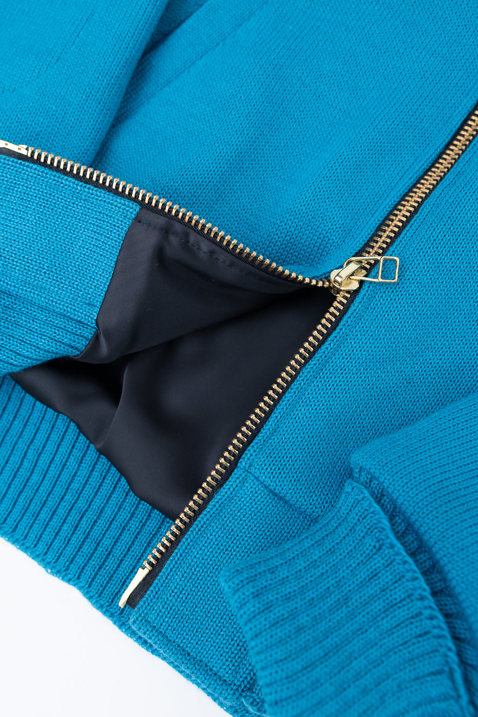 Close-up of aqua full-zip moto hoodie front, showing gold zipper, ribbed hem, and fabric texture.