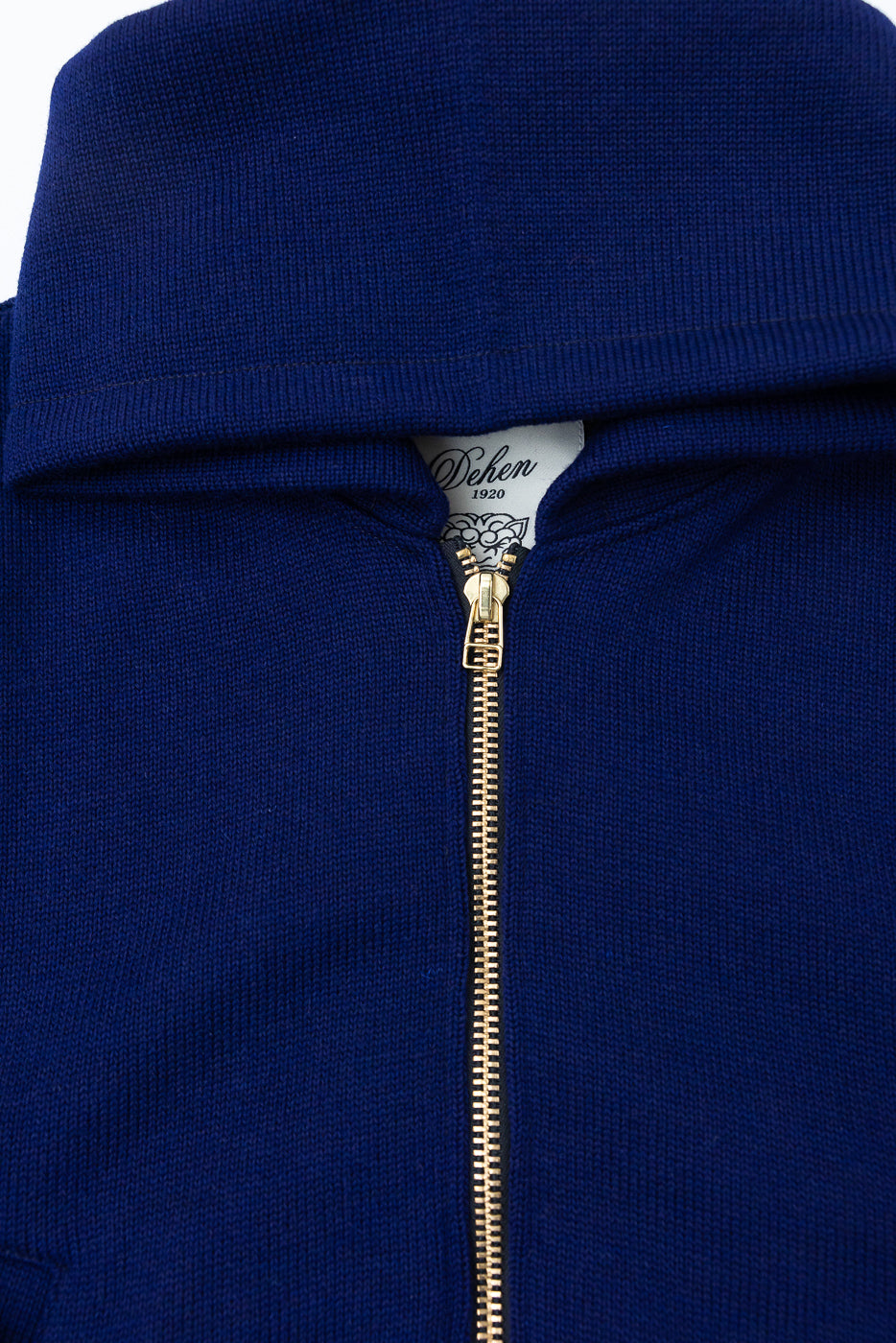 Close-up of the front upper chest and collar of a purple full-zip hoodie showing gold zipper, ribbed knit texture, and branded neck tag.