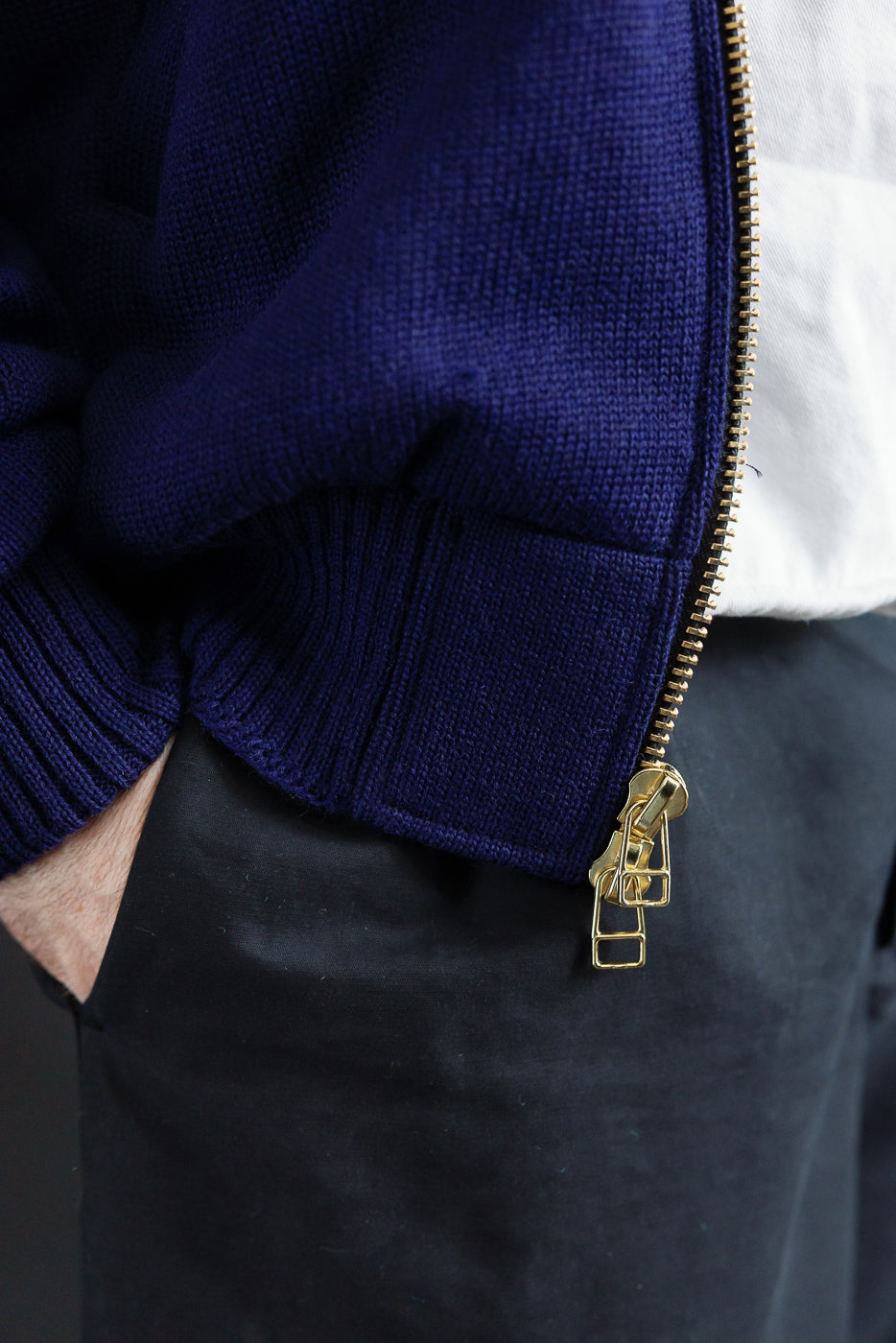 Close-up of lower front zipper, ribbed hem, and fabric texture on purple full zip moto hoodie worn by male model, 5'9
