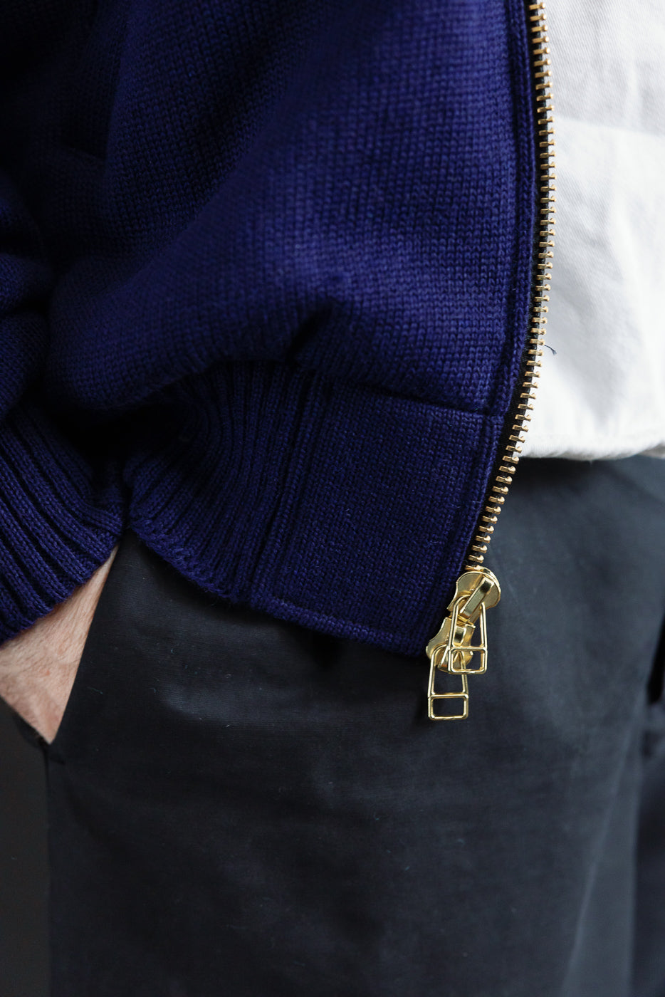 Close-up of lower front right side of purple full-zip moto hoodie showing gold zipper and ribbed knit hem, worn by male model, 5'9
