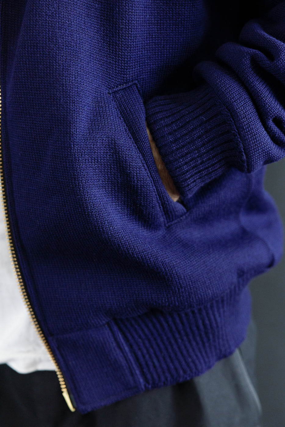 Close-up of male model's hand in front pocket of purple full-zip moto hoodie, showing ribbed cuffs and textured fabric, left side view.
