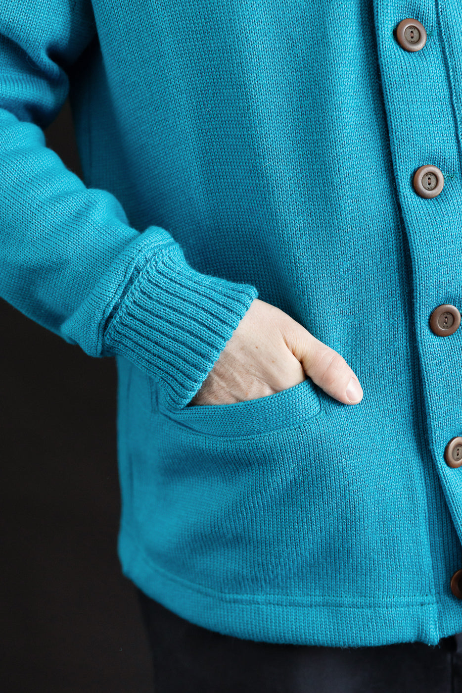 Close-up of front of aqua shawl sweater coat, showing ribbed cuff, brown buttons, and pocket detail on male model, 5'9
