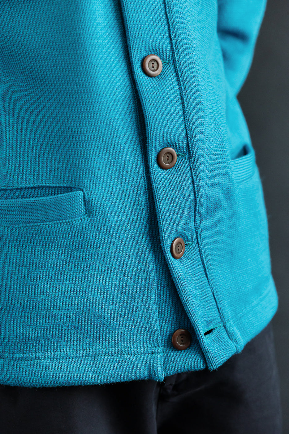 Close-up of aqua men's shawl sweater coat front, showing button details and pocket.
