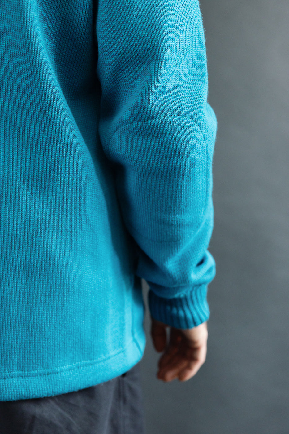Close-up of male model's right sleeve and side in aqua knit shawl sweater coat, showing ribbed cuff and fabric texture. Model is 5'9