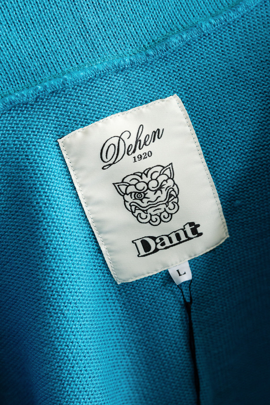 Close-up of interior neck tag on aqua shawl sweater coat, showing fabric texture and brand label.
