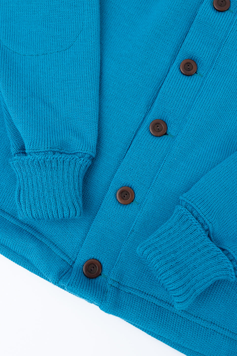 Close-up of front lower section of aqua blue knit shawl sweater coat, showing ribbed cuffs, button details, and textured fabric.