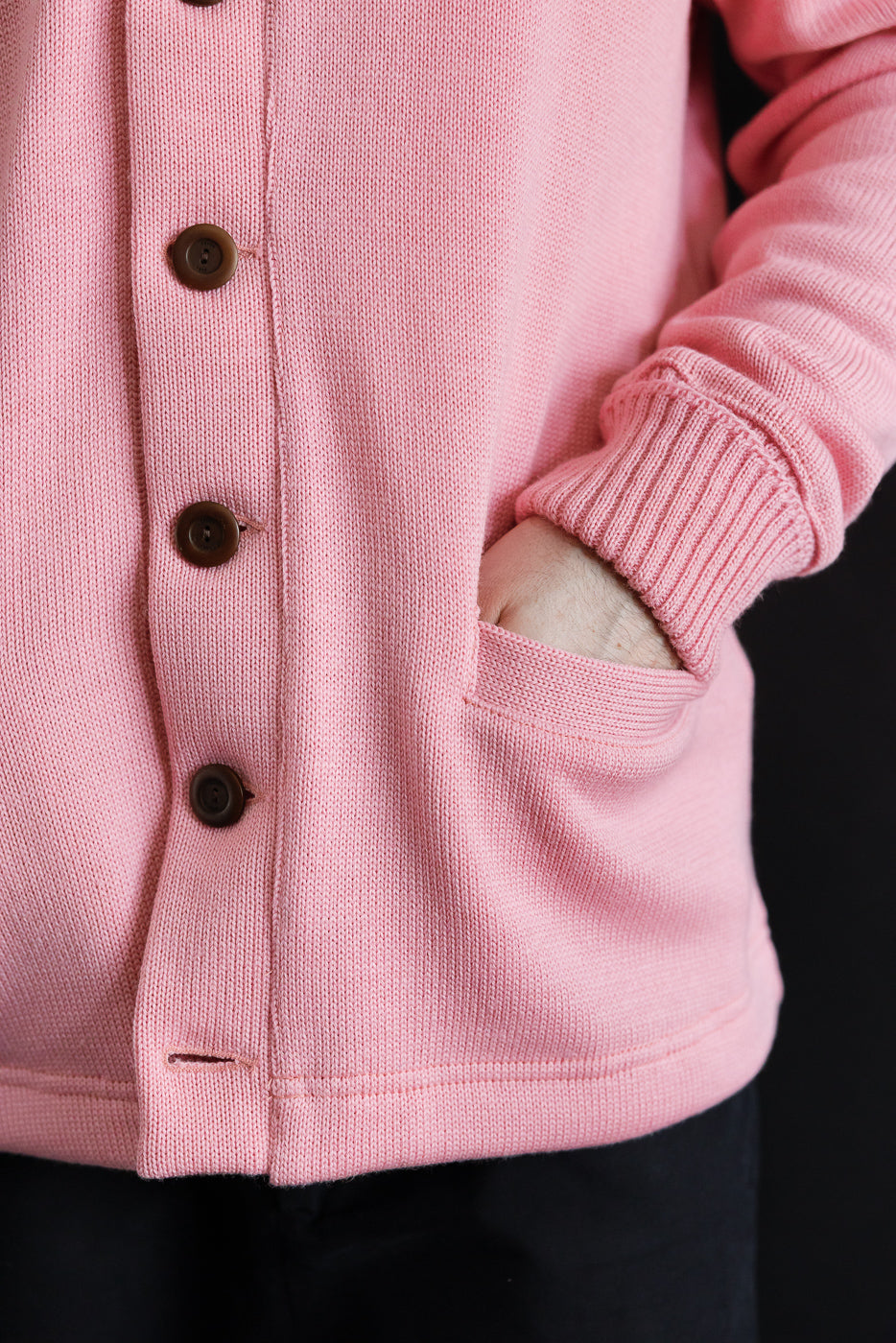 Close-up of male model's hand in front pocket, bubblegum pink shawl sweater coat, showing buttons and knit texture.