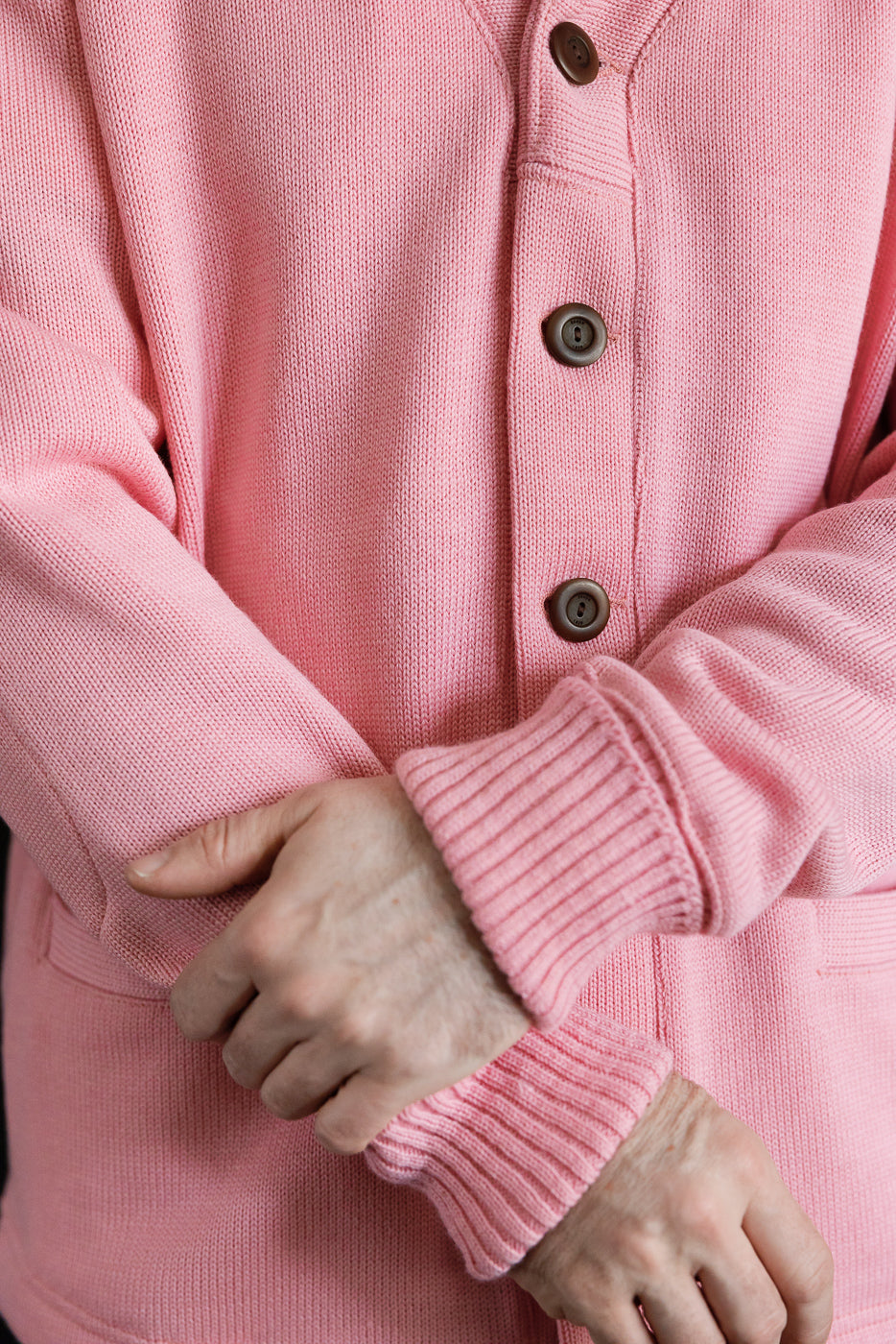 Close-up front of men's pink shawl sweater coat, showing buttons, ribbed cuffs, model is male, 5'9