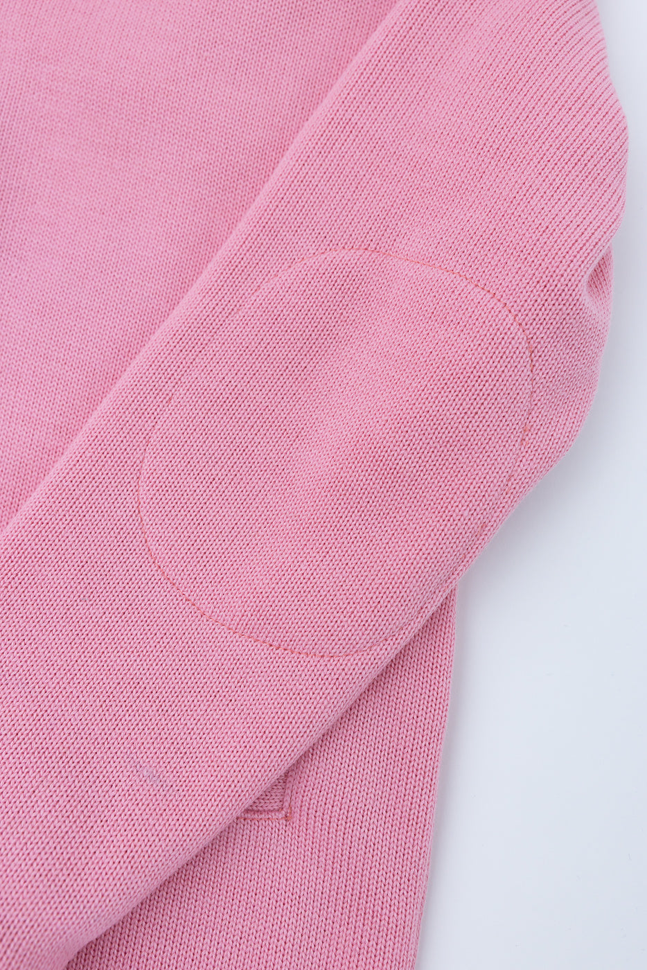 Close-up of pink knit shawl sweater sleeve showing oval elbow patch detail and textured fabric.