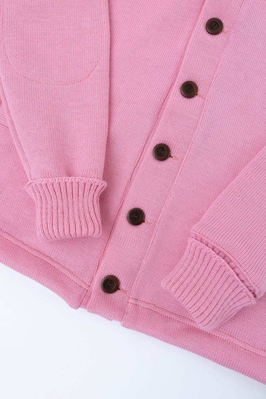 Close-up of front of pink shawl sweater coat, showing ribbed cuffs, buttons, and knit texture.