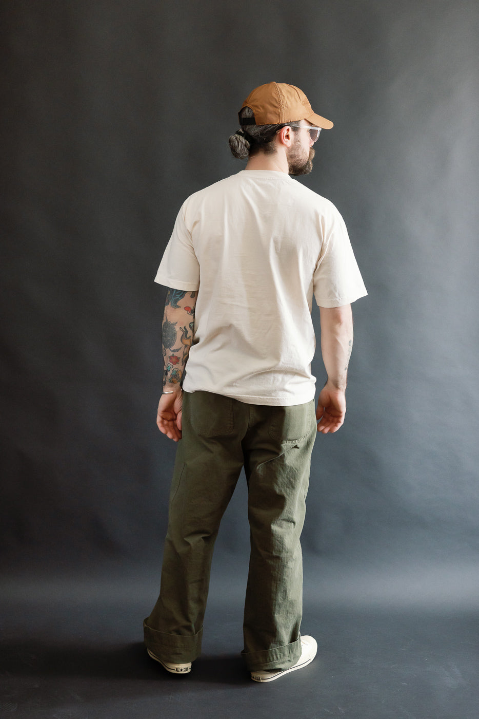 Man in profile wears a 6.5oz - Dant Kingfisher T-Shirt - Ecru, showcasing its oversized, boxy fit. Styled with olive-green pants and off-white sneakers, highlighting the T-shirt's casual, heritage-inspired design.