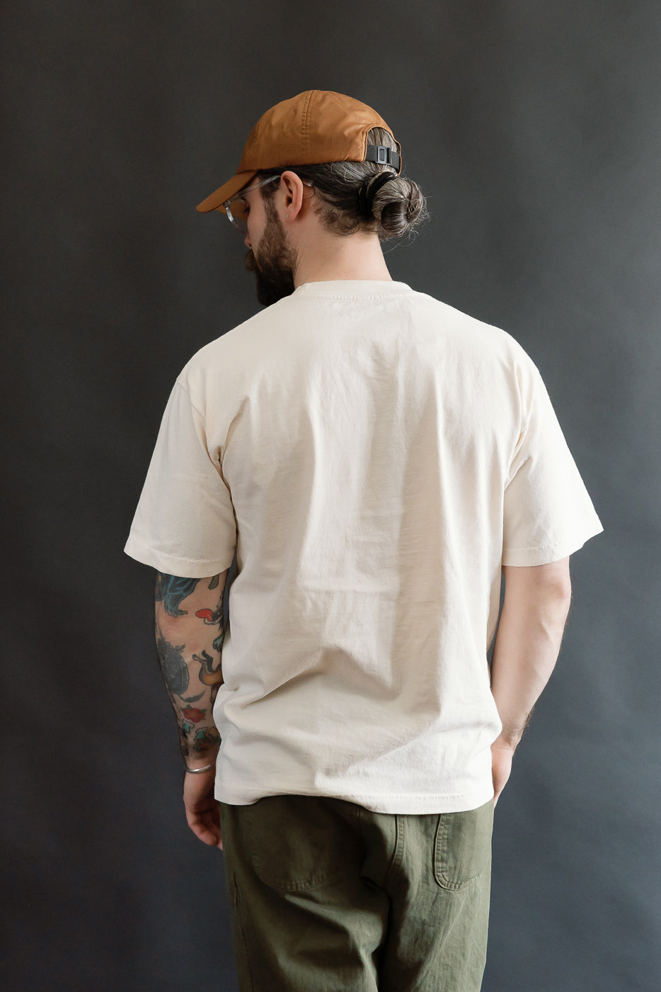 A man models the 6.5oz - Dant Kingfisher T-Shirt - Ecru, showcasing its casual, oversized fit, with vibrant tattoos on display, perfectly embodying Dant's heritage-inspired aesthetic.