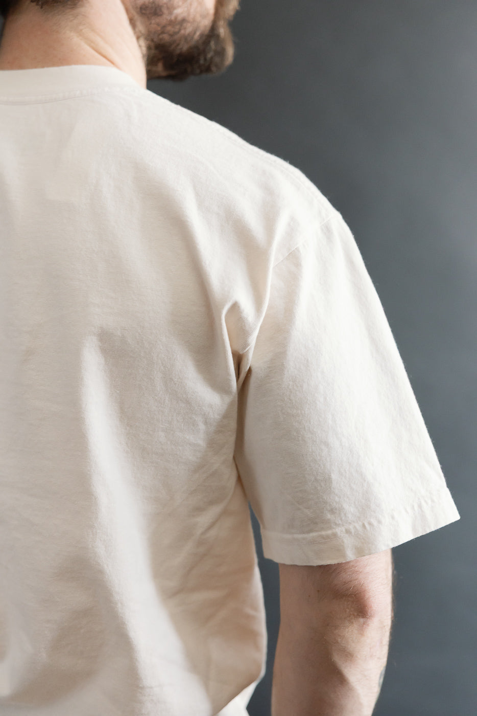 Cropped view of a person wearing the 6.5oz - Dant Northern Flicker T-Shirt - Ecru, showcasing its short-sleeve design and off-white color against a neutral background.