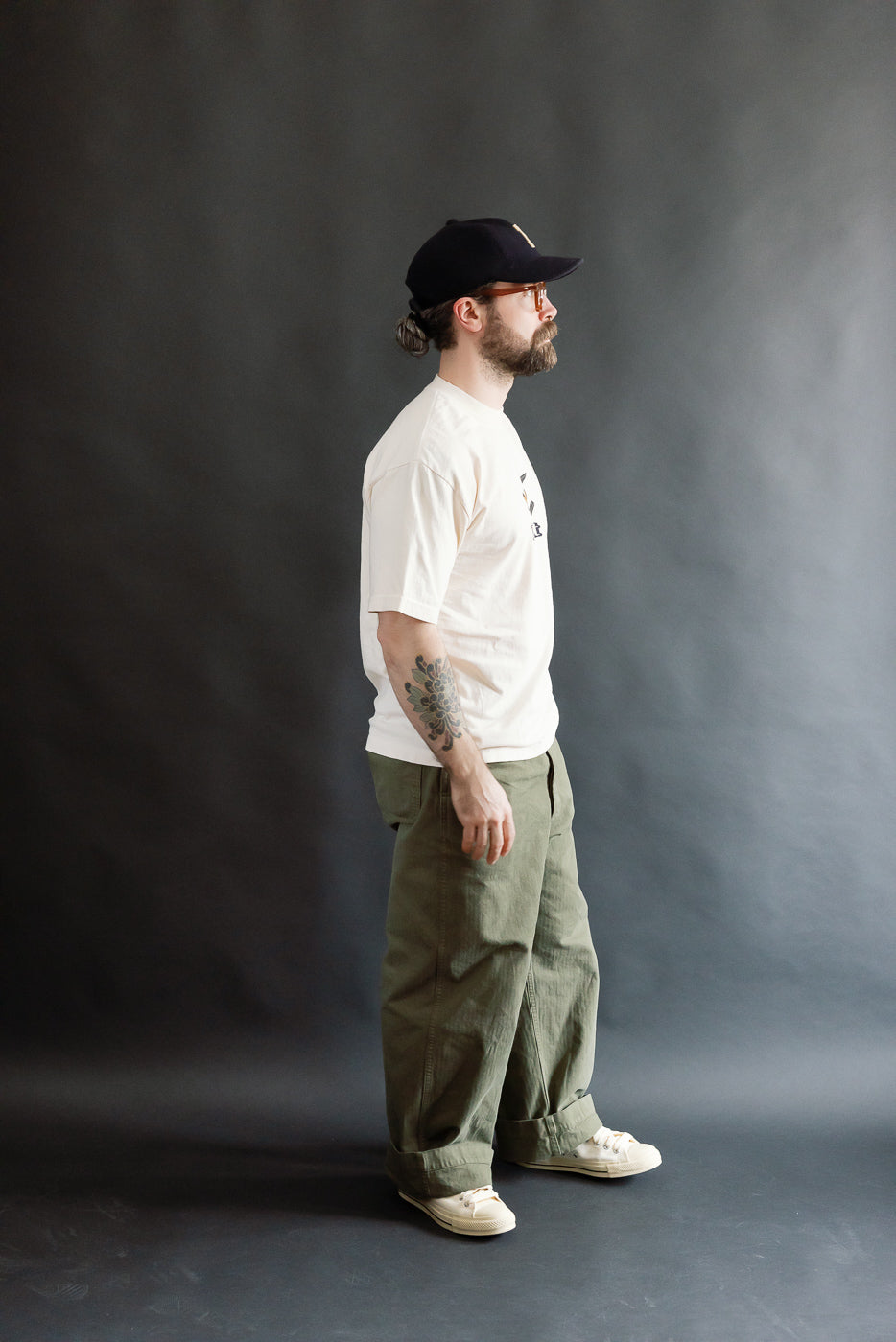 Man in profile wearing the 6.5oz Dant Northern Flicker T-Shirt in Ecru, showcasing its loose fit and casual style, paired with olive-green pants and off-white sneakers, reflecting Dant's heritage-inspired fashion.