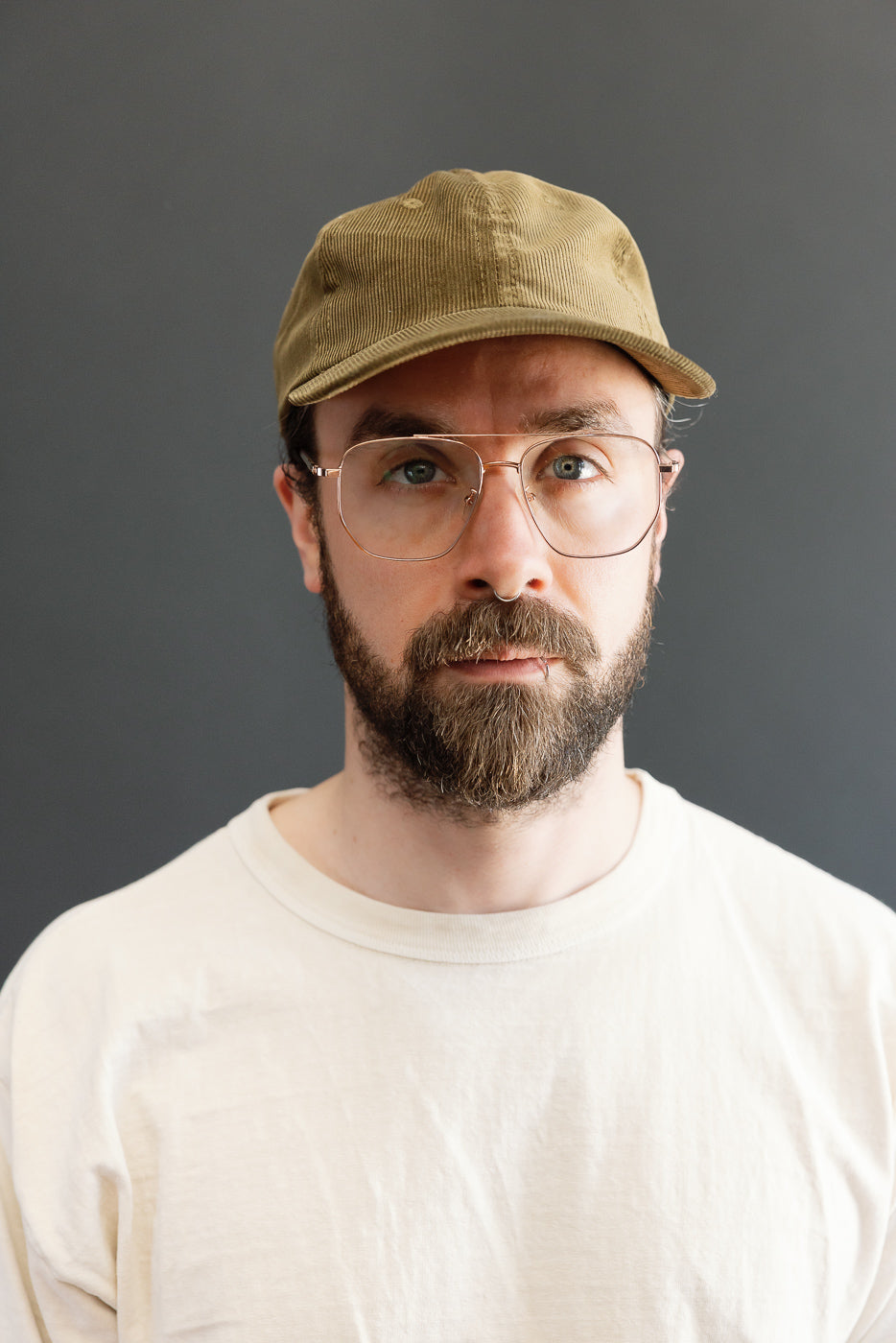 Man with beard and eyeglasses wearing a Corduroy Baseball Hat - Olive in tan corduroy, featuring a 6-panel unstructured crown, pre-curved brim, and adjustable leather strap with brass hardware.