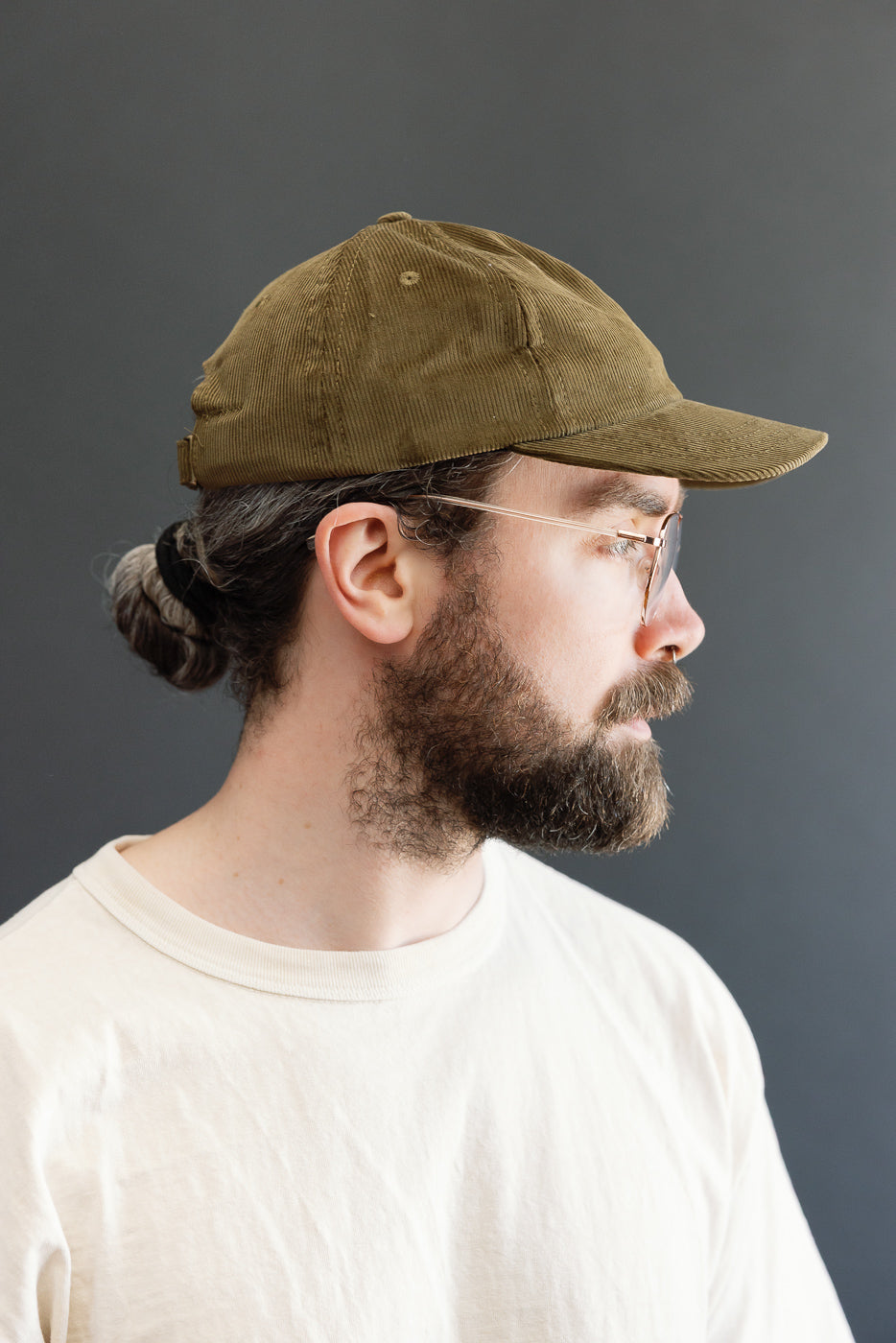 Corduory Baseball Hat - Olive: Side profile of a man wearing an olive-green, unstructured baseball cap made from soft, thin-wale corduroy, featuring a pre-curved brim and adjustable leather strap with brass buckle.