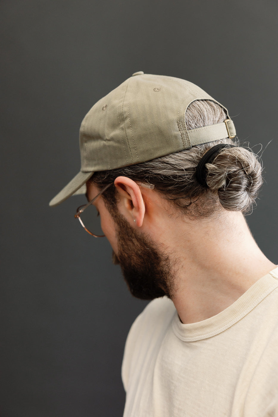 Back and side view of a man wearing the Dry Wax Cotton Baseball Hat - Sage by Dehen, showcasing its unstructured six-panel design, flat brim, and self-fabric adjustable strap with antique brass slider.