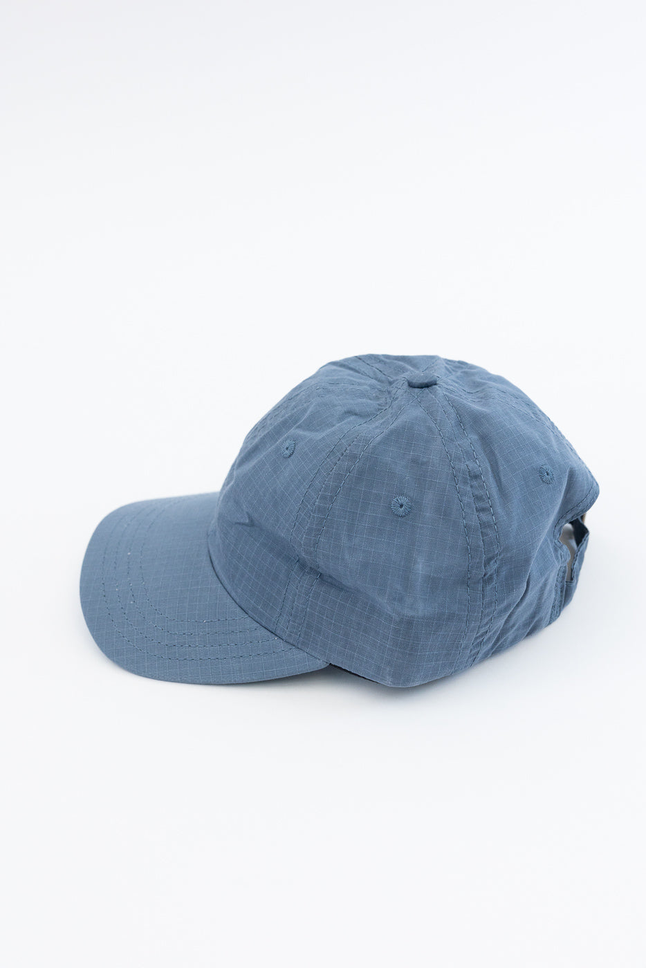 Close-up flat lay of faded blue ripstop cotton baseball hat, front left side view.