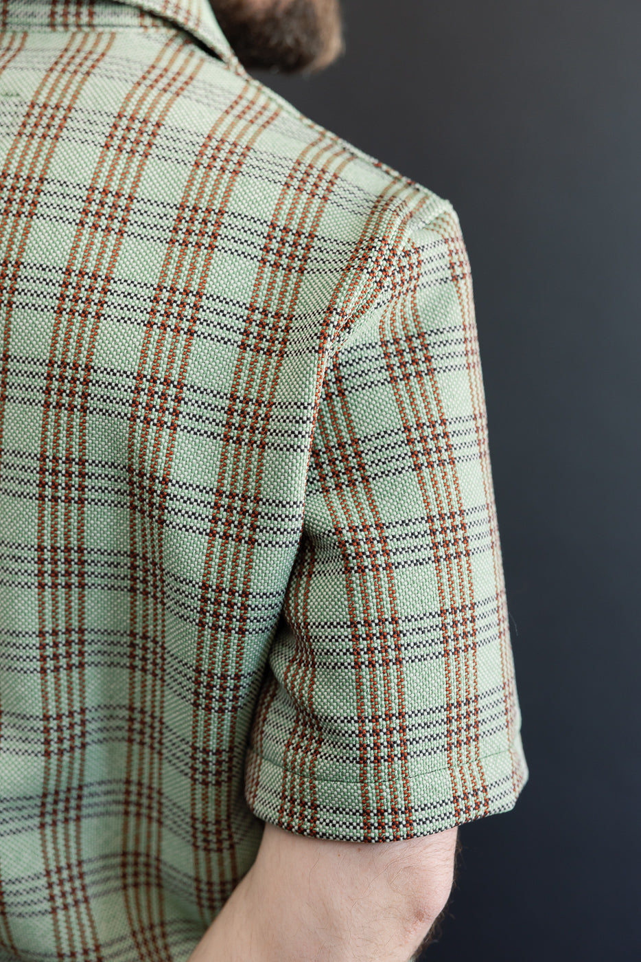 Close-up of male model's right side in green plaid lounge shirt, showing fabric texture and sleeve detail. Model is 5'9