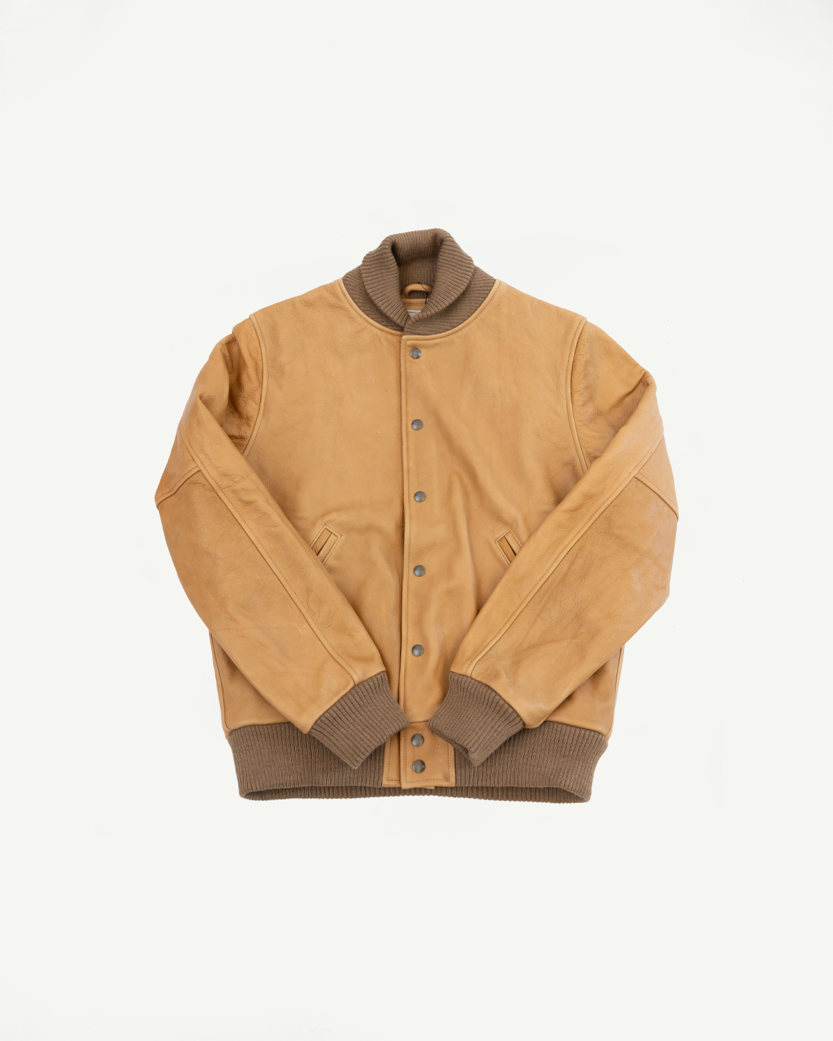 Flat lay of tan leather varsity jacket, front side, snap buttons, ribbed collar, cuffs, and hem.