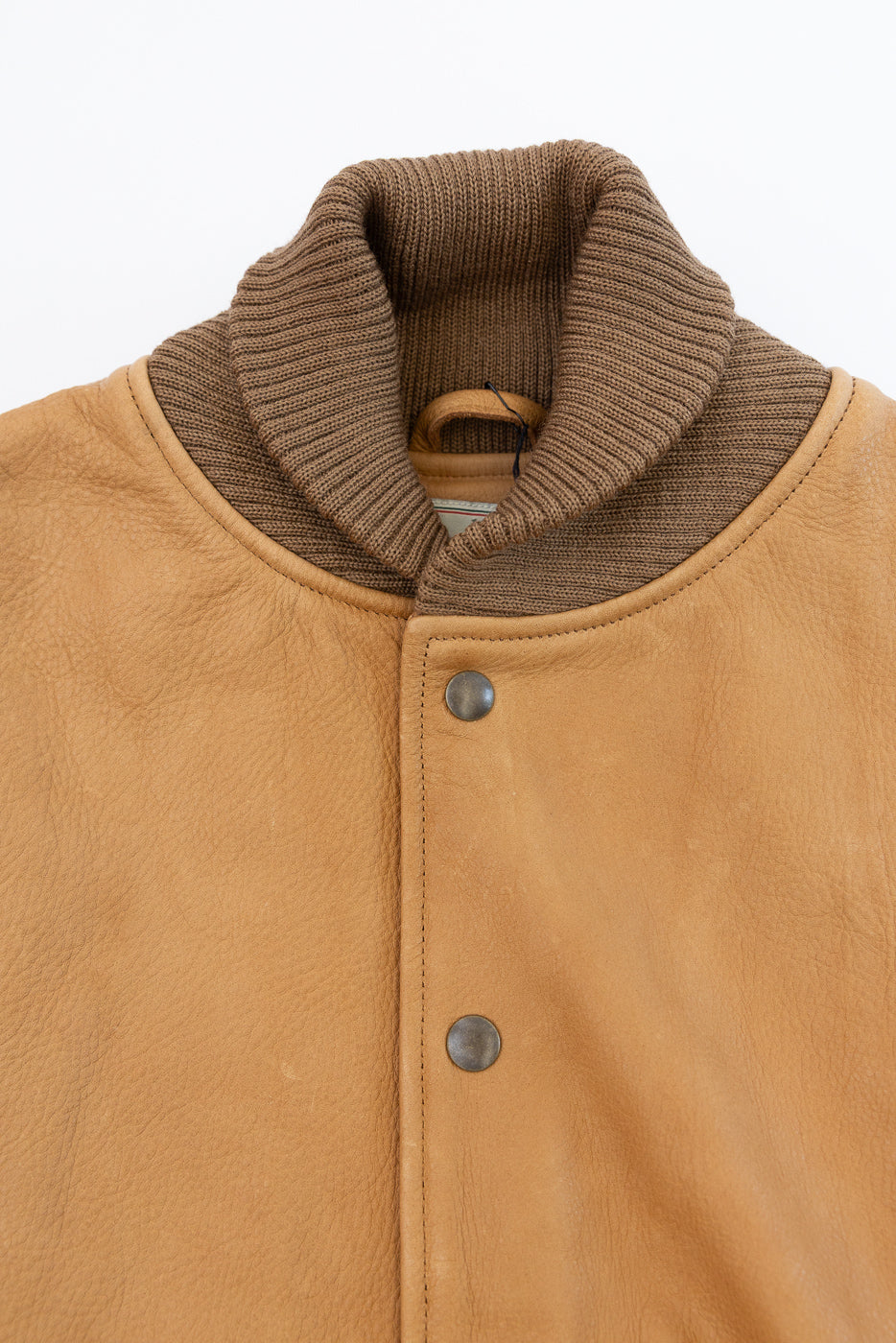 Close-up of front upper chest and collar of tan leather jacket, showing ribbed knit collar, snap buttons, and leather texture.