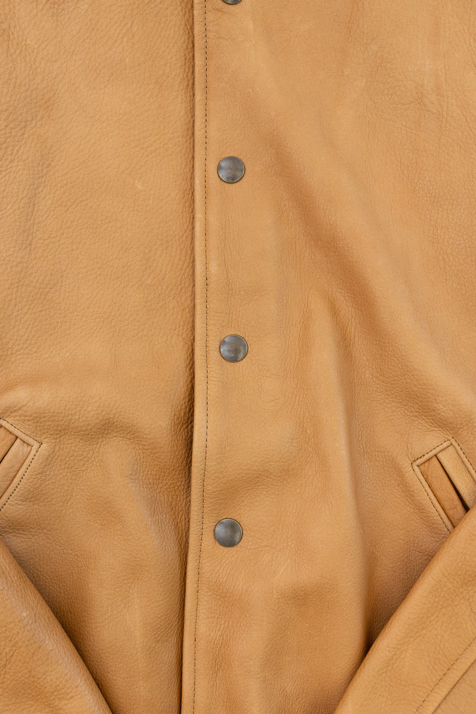 Close-up of front center of tan leather jacket showing snap buttons, pocket details, and grain texture
