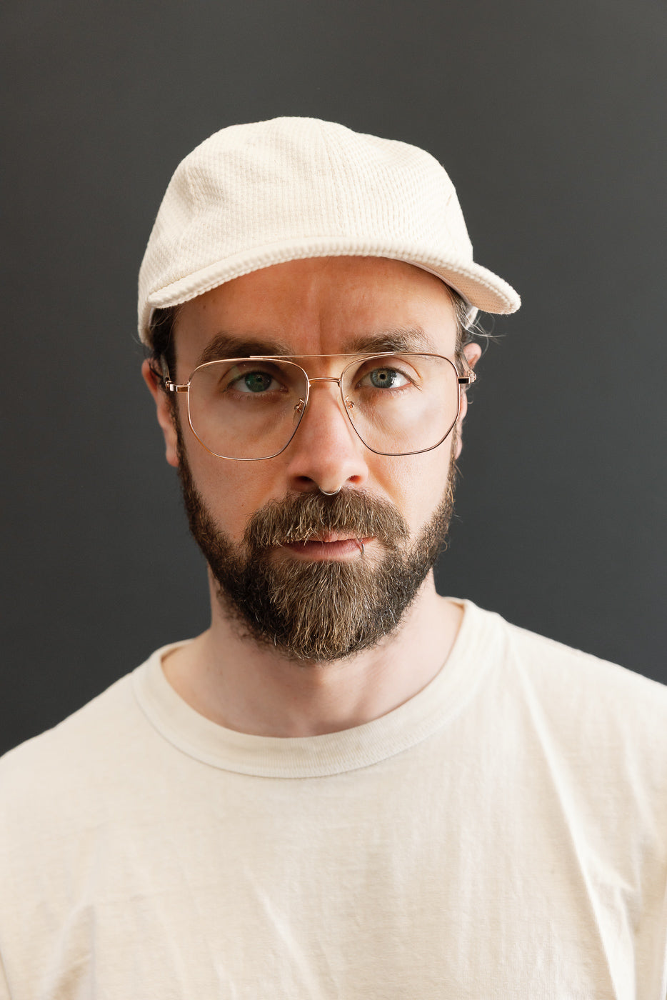 Sashiko Cotton Baseball Hat - Natural worn by a bearded man, showcasing its unstructured 6-panel design and adjustable strap with brass buckle, highlighting the craftsmanship of Japanese and American workwear influences.