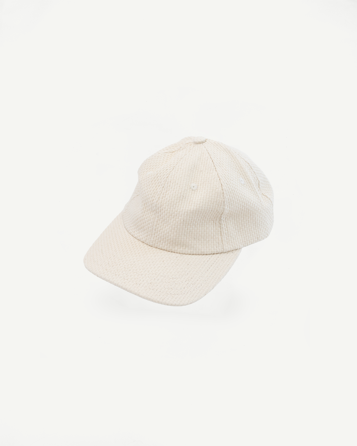 Sashiko Cotton Baseball Hat - Natural: An off-white, unstructured six-panel cap crafted from natural sashiko cotton, featuring a waffle texture, curved brim, and adjustable leather strap with brass buckle.