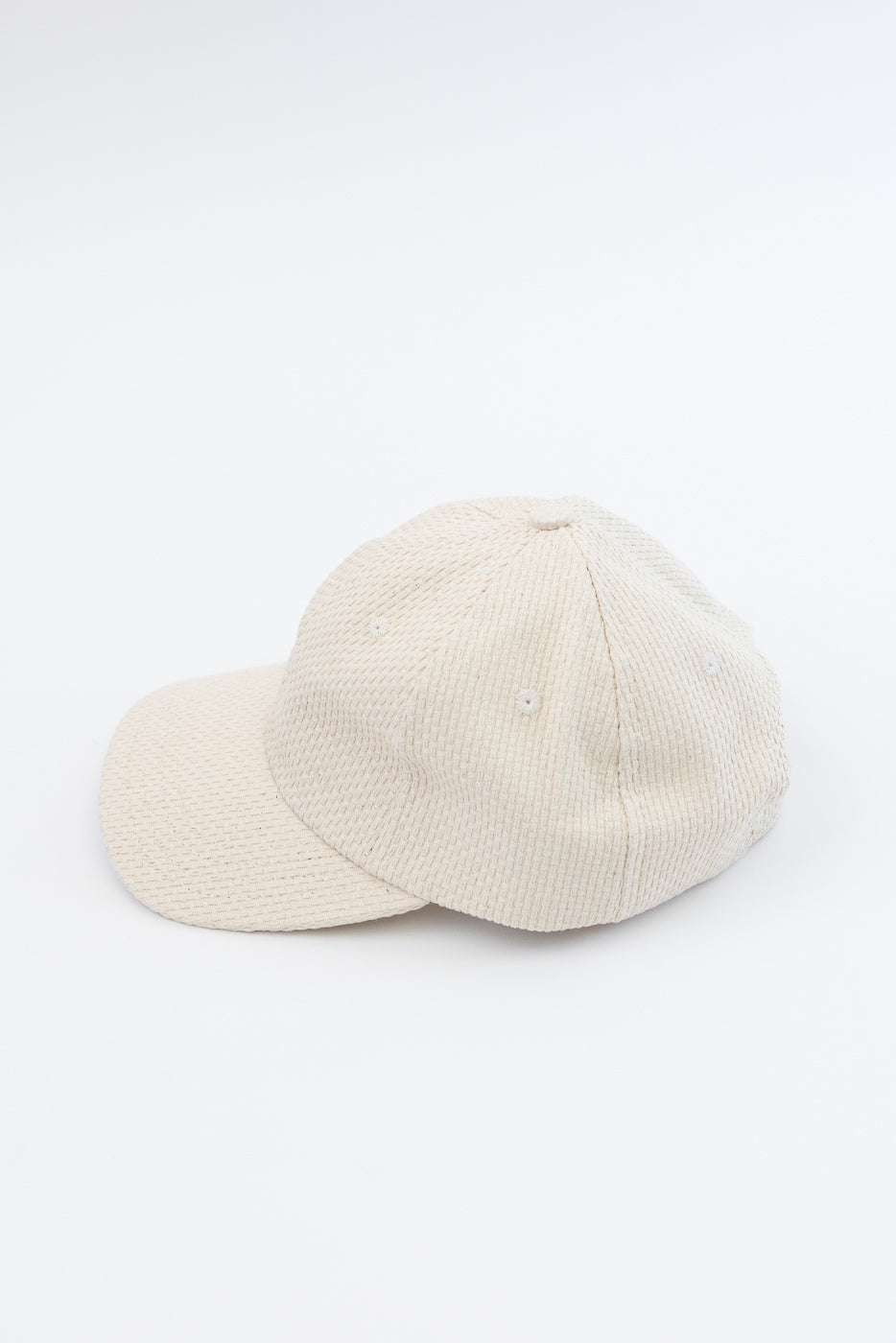 Sashiko Cotton Baseball Hat - Natural, a light-beige six-panel cap crafted from textured sashiko cotton, features a pre-curved brim, leather strap with brass buckle, and unstructured crown on a white backdrop.