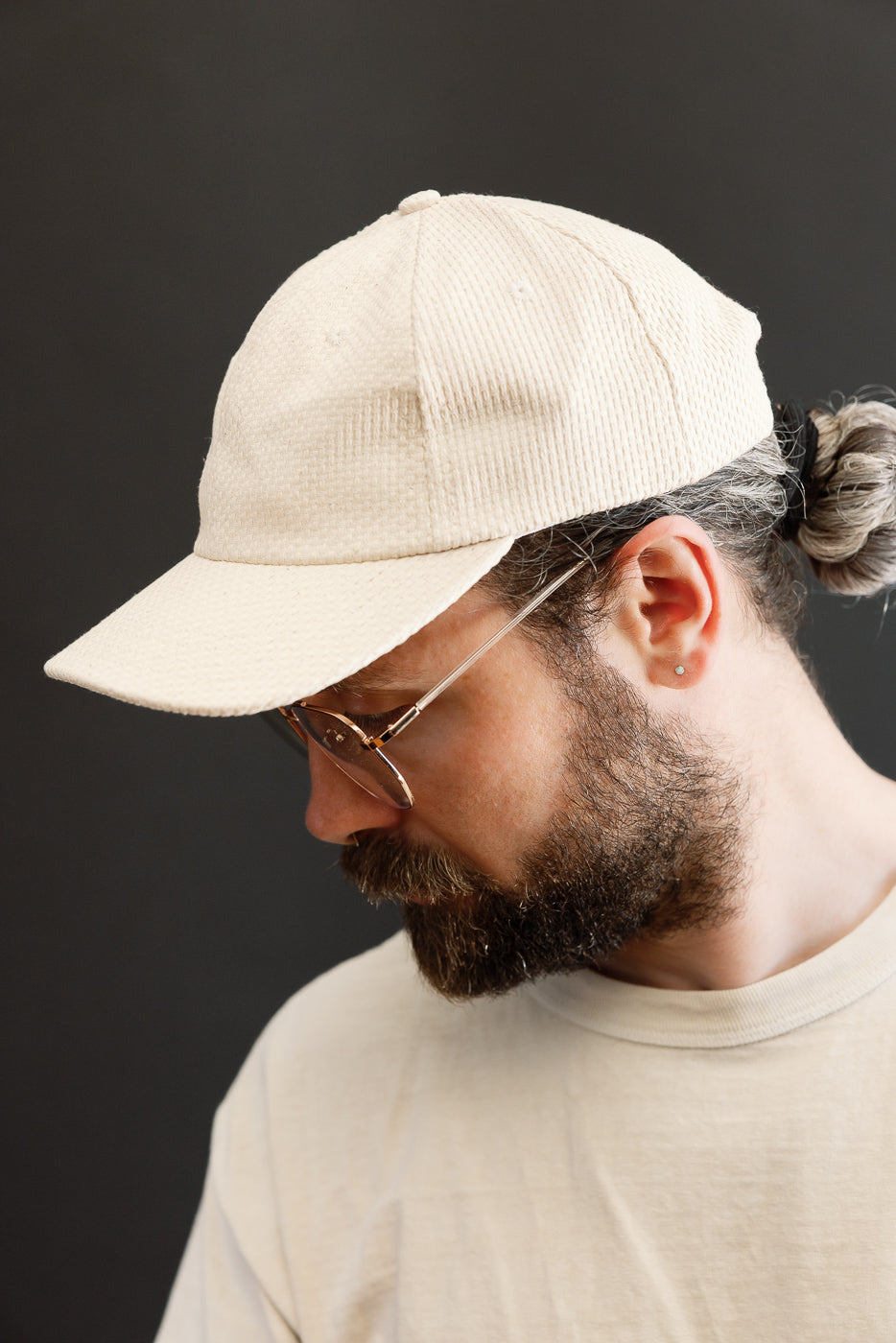 Sashiko Cotton Baseball Hat - Natural worn by bearded man in profile, showcasing its unstructured design and fine grid stitching, paired with a light-colored T-shirt, against a dark backdrop.