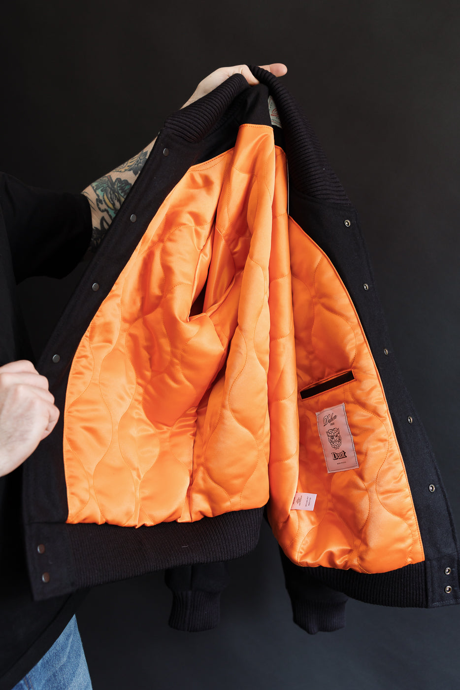 a man holding the jacket up in the air to show of the orange satin onion quilted liner and Dehen x Dant woven label