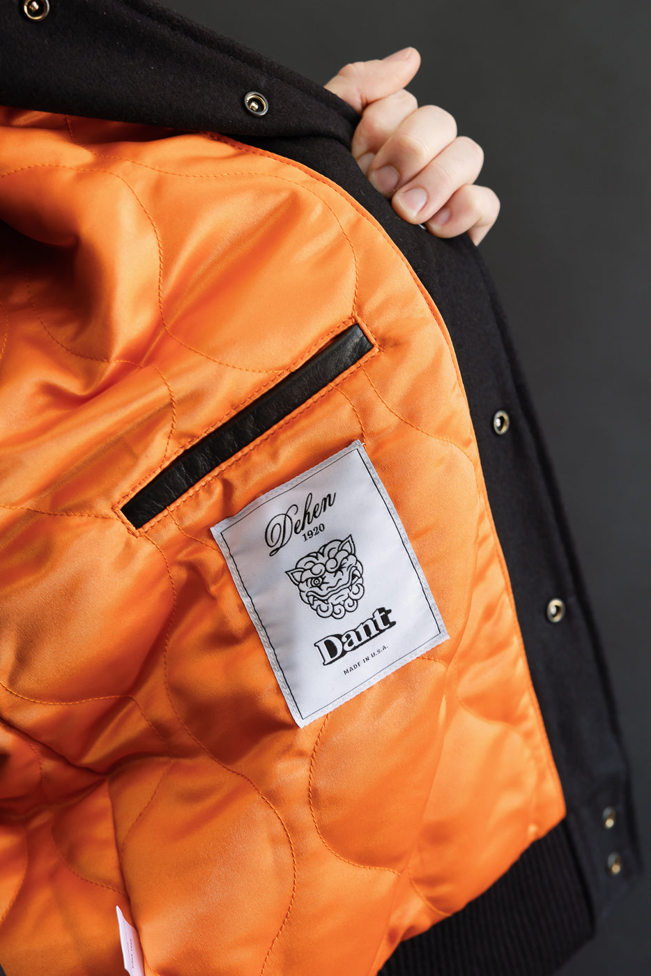 close up of leather interior welt pocket against orange sating onion quilted lining with white dehen x dant woven label below pocket