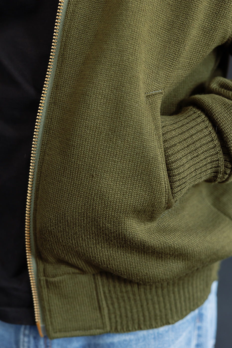 close up of olive green knitted hoodie welted pocket with hand in it