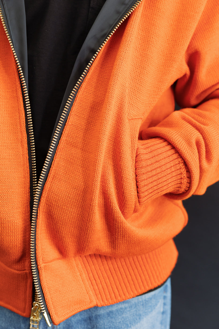 Male model wearing a knitted orange hoodie (open), black shirt, close up, hands in pockets