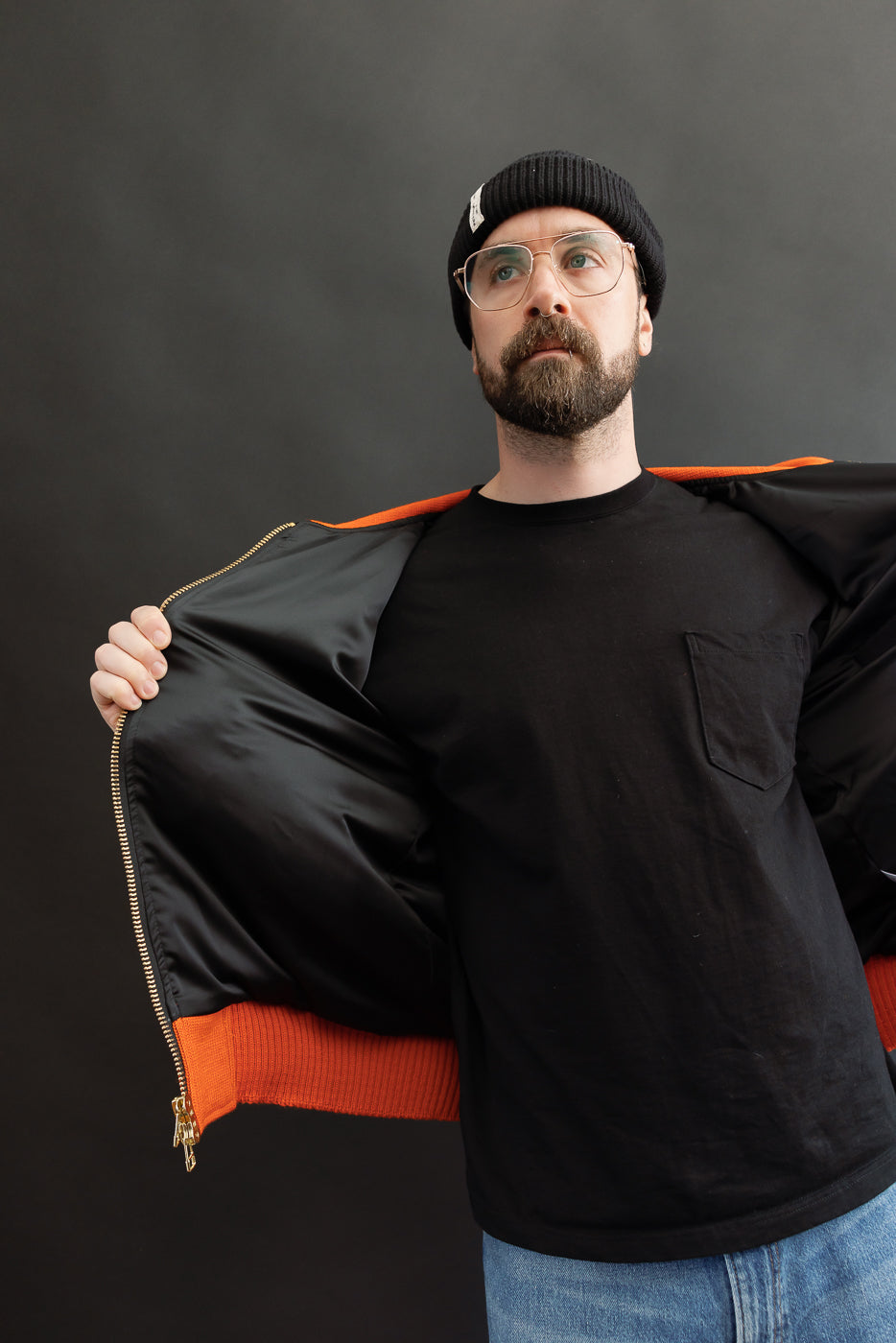 Male model wearing an orange jacket with black lining open, 3/4 length
