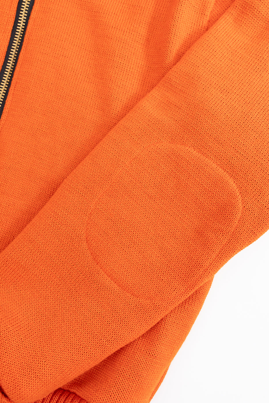 close up of stitching for interior elbow pad on orange knit jacket