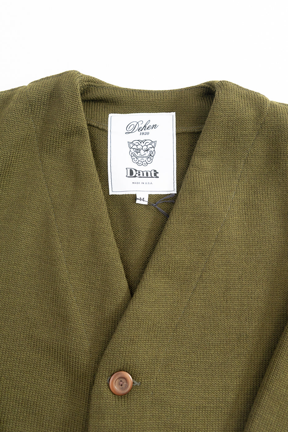 Green cardigan with brown buttons on a white background, close up on white woven dehen x dant collaboration tag