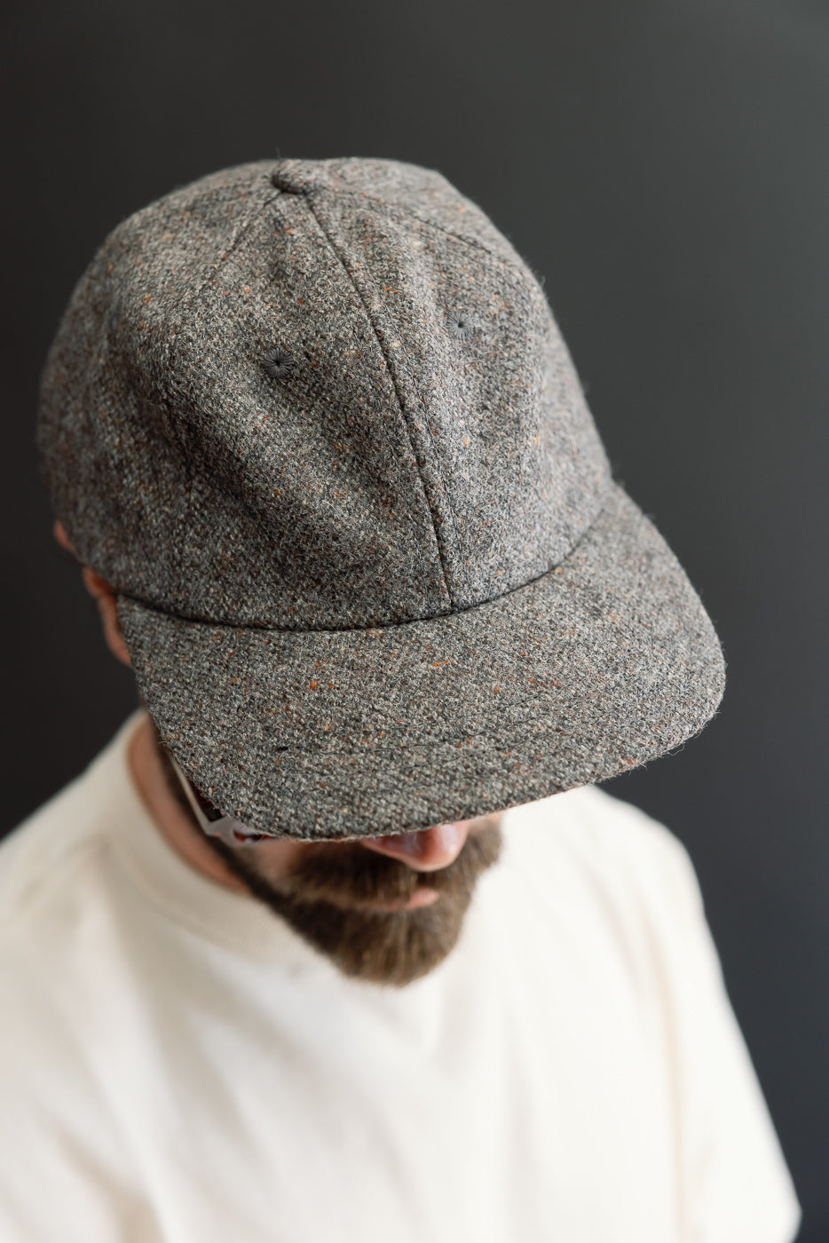 Close-up of the front of a grey textured tweed baseball cap worn by a male model, 5'9