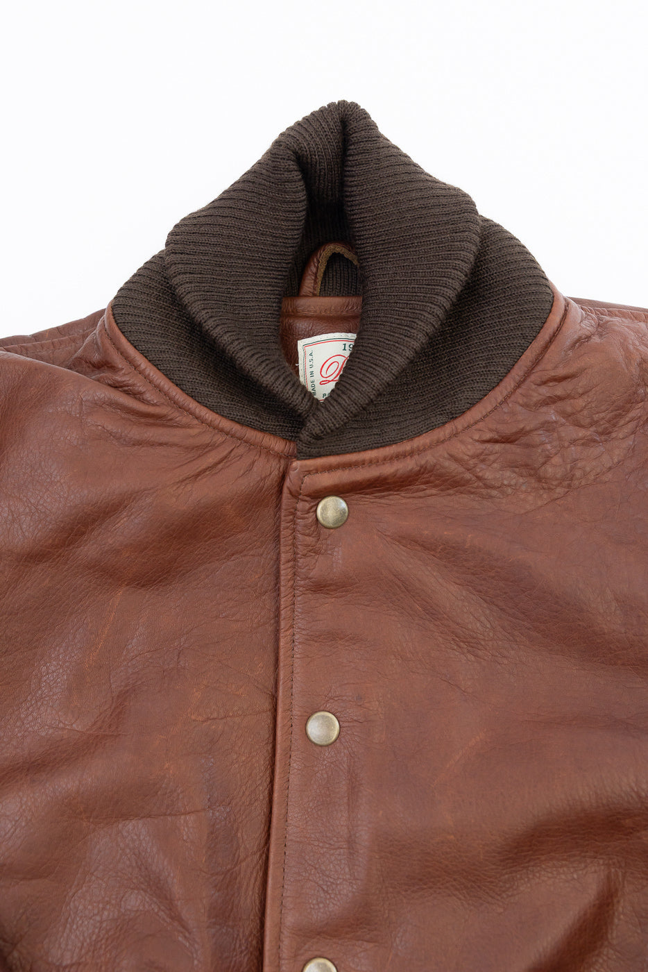 Close-up of the front collar, ribbed knit neckline, and button detail of a brown leather jacket.