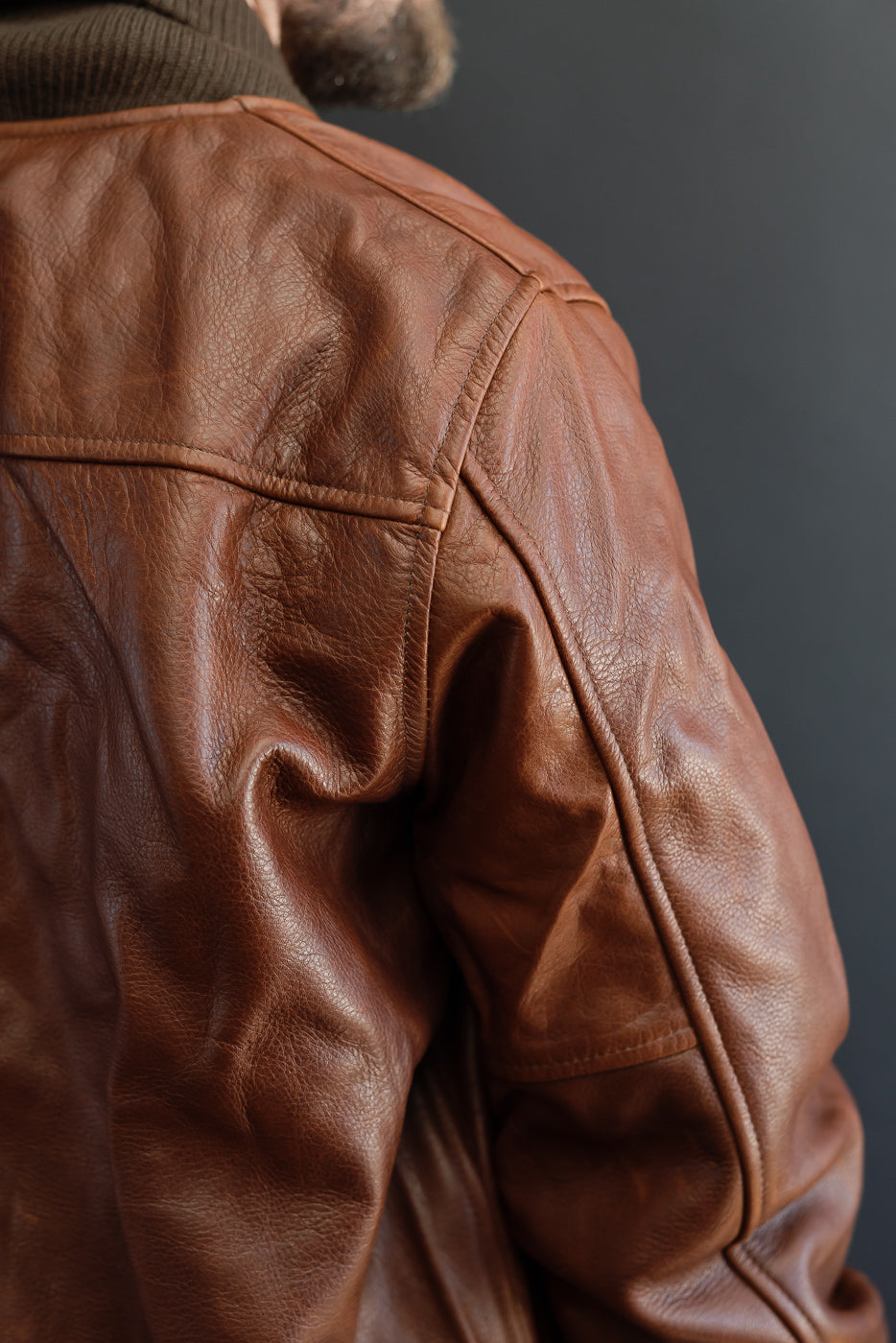 Close-up back view of a brown leather jacket showing shoulder seam and textured grain.