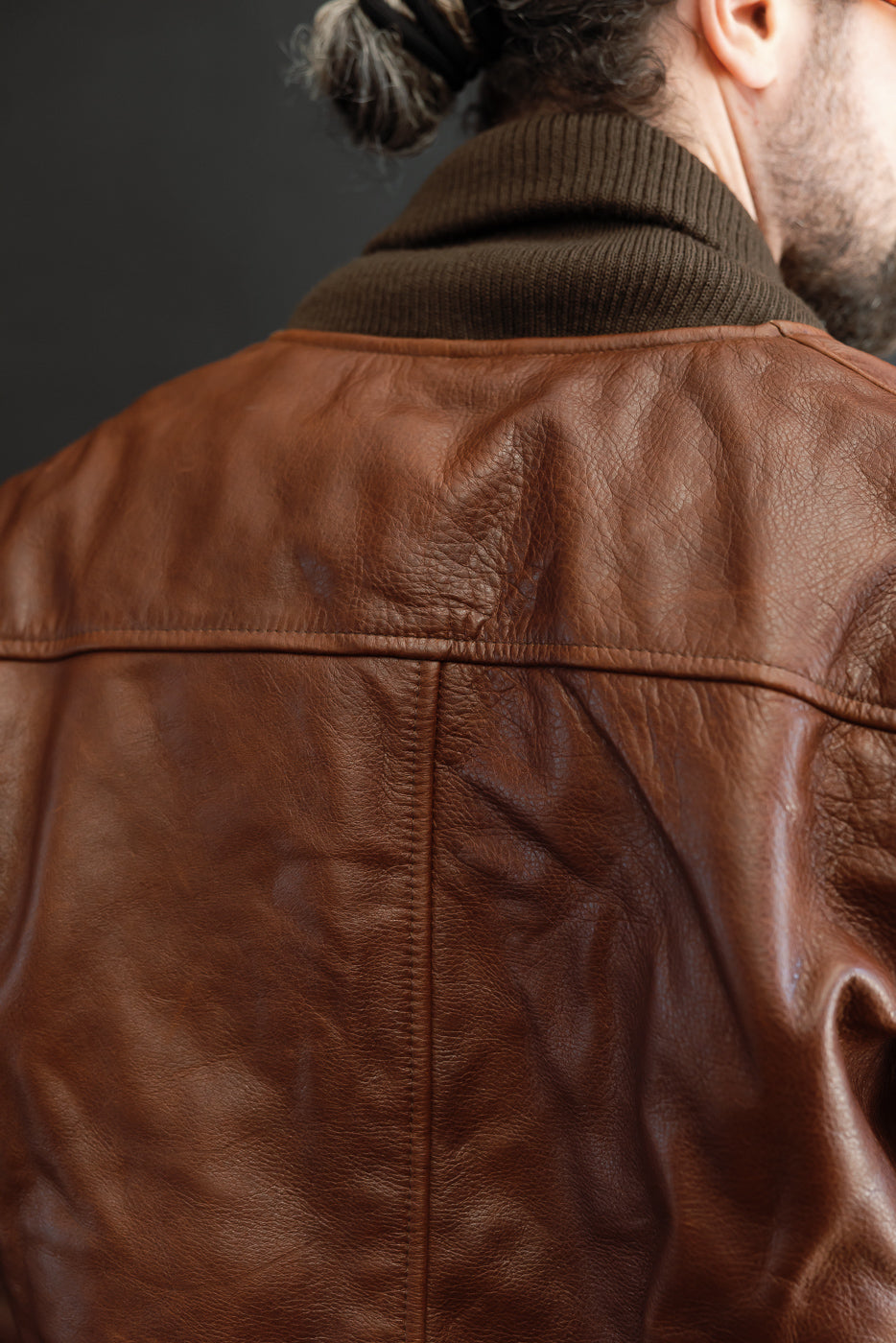 Close-up back view of a brown leather jacket's texture and seam on a male model.