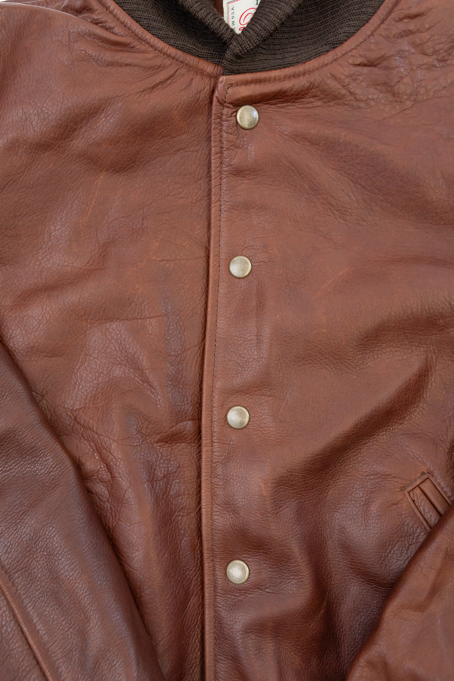 Close-up of the front of a brown leather jacket showing the texture and silver snap buttons.