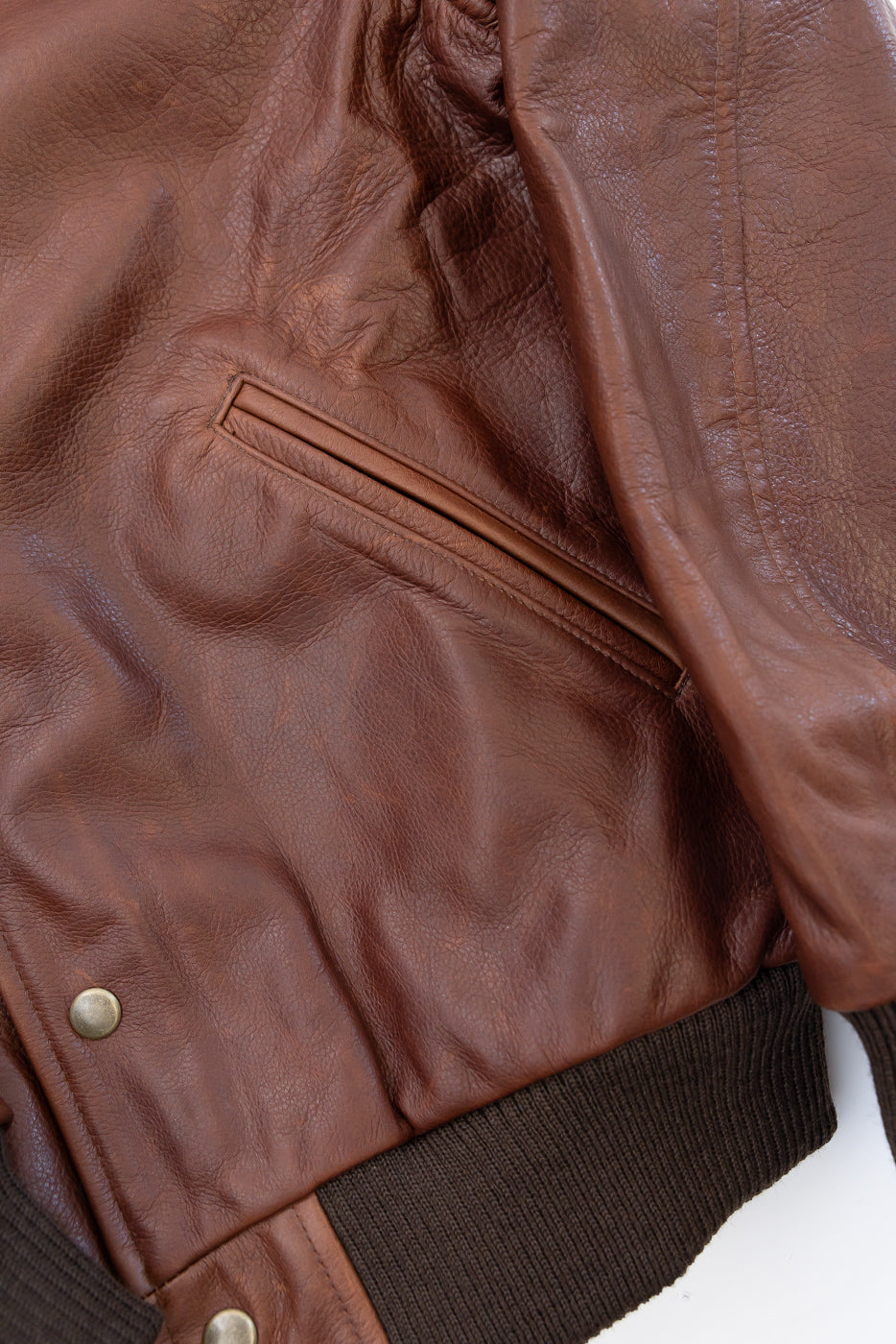 Close-up of the front side showing the slanted welt pocket and pebbled texture of a brown leather jacket.
