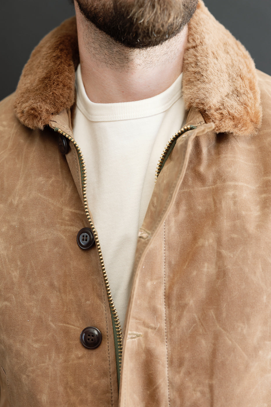 Close-up front view of a tan faux-fur collar and button detail on a canvas jacket.