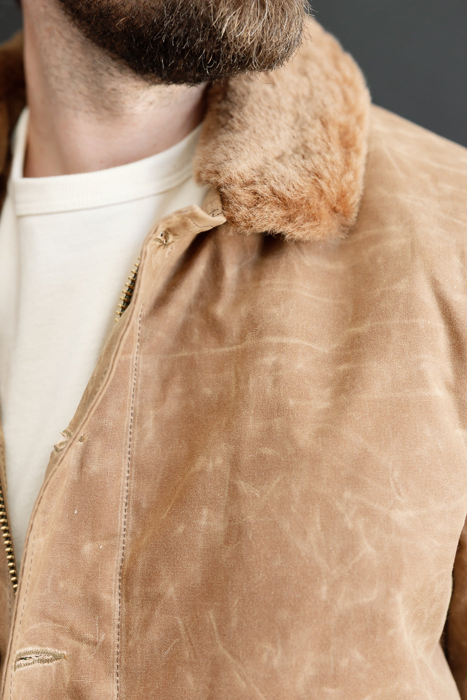 Close-up of the front right collar and chest of a tan faux-shearling jacket on a male model.