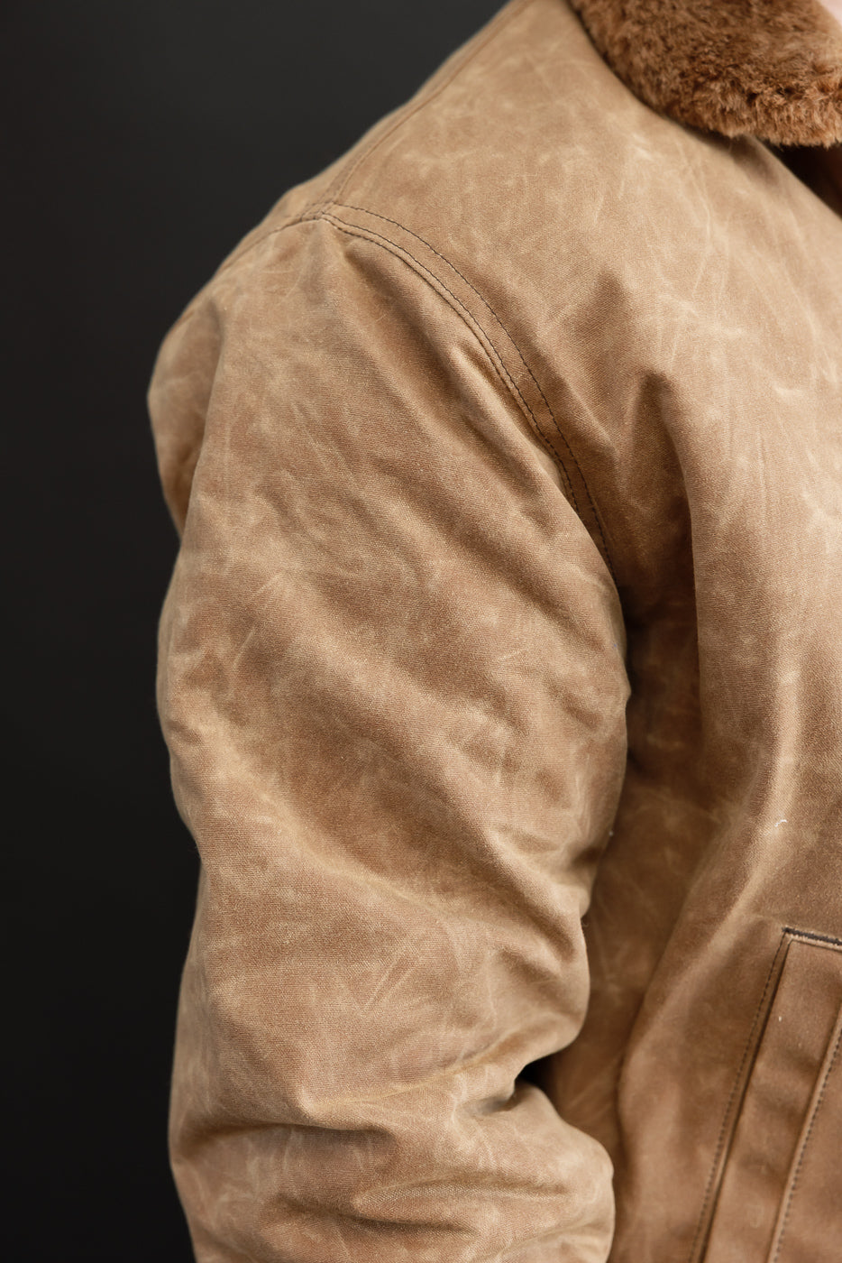 Close-up of a male model's right sleeve and side of a brown waxed canvas jacket with fur collar.